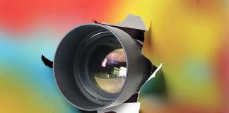 camera lens emerging through torn paper on colorful background