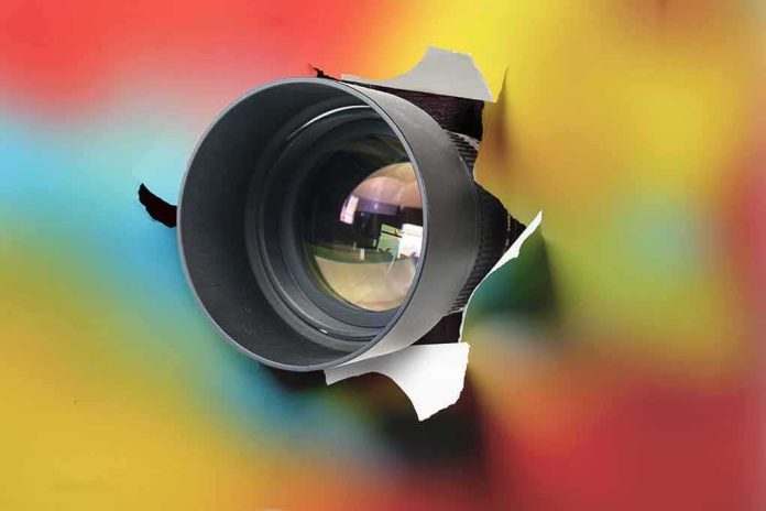 shutterstock_1892209375 camera lens emerging through torn paper on colorful background