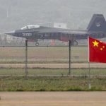 Why China Could OUTGUN Our F-35 Pilots Stealth fighter jet on runway behind fence with Chinese flag in foreground