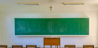 Empty classroom with green chalkboard and wooden desks