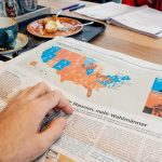 State Now REQUIRED to Say ‘Gulf of America’ Hand holding newspaper with US election map at a cafe table
