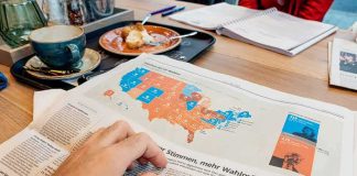Hand holding newspaper with US election map at a cafe table